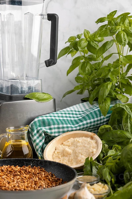 Ingredients for pesto such as basil, sunflower seeds, olive oil and parmesan next to a blender