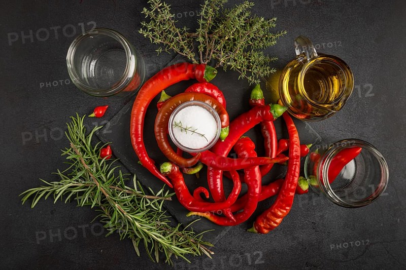 Hot red peppers with vinegar, oil, salt and herbs on a black background