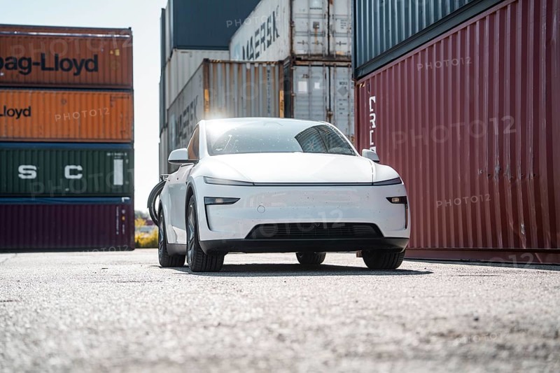 White car in a harbour environment next to stacked freight containers, Tesla Model Y Juniper, electric car