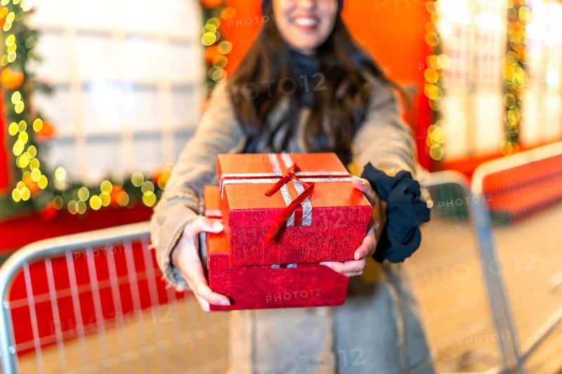 Woman holding christmas presents at a festive market, smiling brightly while sharing the joy of giving during the holiday season