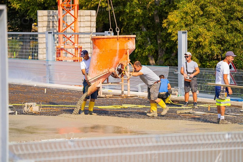 Workers pouring concrete with a shaking bucket on a sunny construction site, car park construction, Calw, Germany