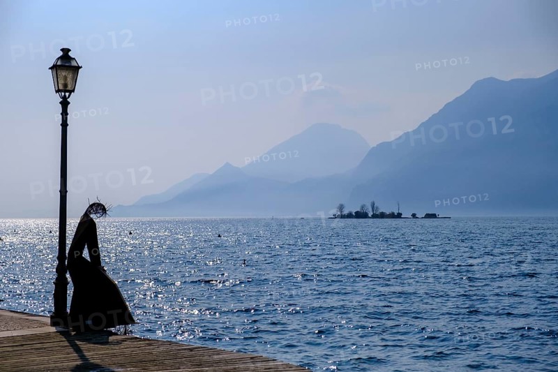 Sculpture of a fisherwoman at the harbour of Cassone di Malcesine, in the background Isole di Trimelone, Lake Garda, Veneto, Italy