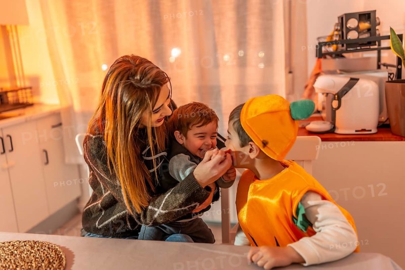 Children wearing pumpkin costumes celebrating halloween joyfully with their mother at home, creating warm memories of togetherness and laughter