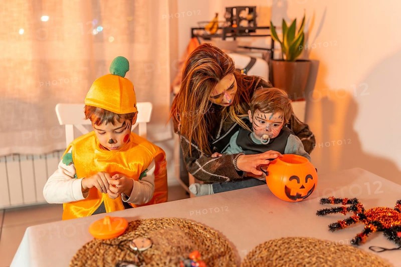 Mother and children wearing festive halloween costumes, joyfully preparing treats together at home, surrounded by autumn decorations and candy