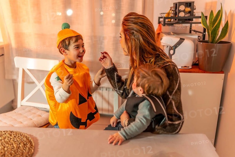 Mom applying halloween makeup on her kid's face, while holding her baby, preparing for trick or treating