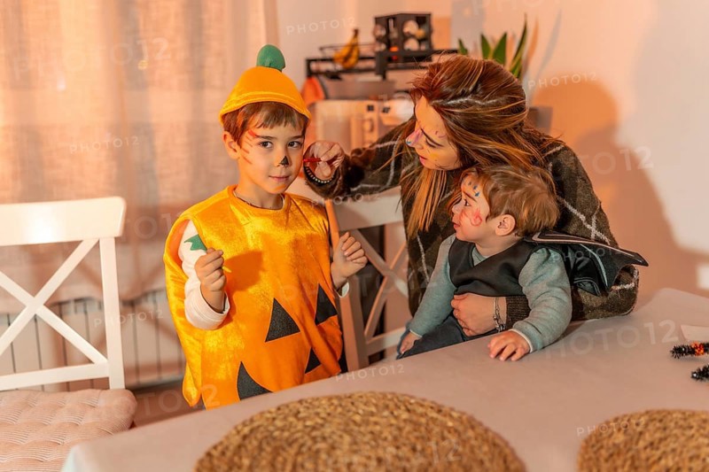 Mother painting her children's faces with halloween makeup, preparing for trick or treating