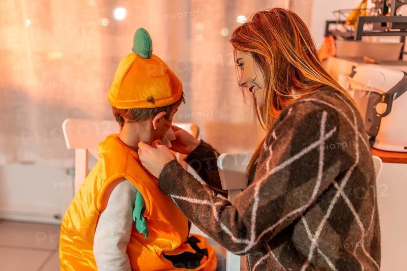 Mother adjusting her son's pumpkin costume, preparing for a festive halloween party at home with joy and excitement filling the air