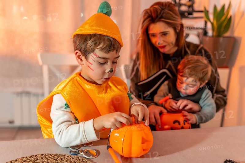 Children wearing halloween costumes are decorating pumpkin baskets with their mother at home