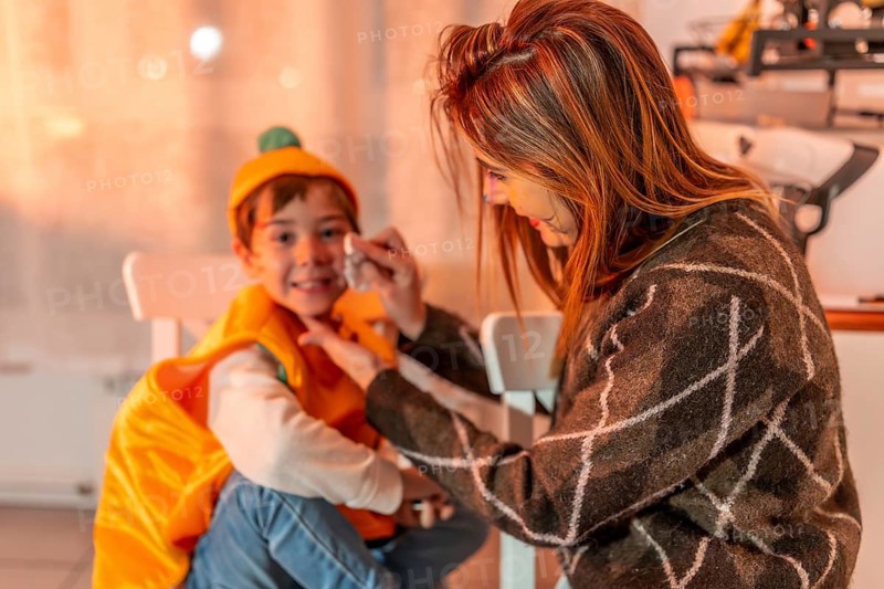 Mom applying colorful makeup on her son's face, creating a festive atmosphere for their halloween party at home, filled with joy and excitement
