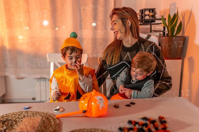 Mother and her two children wearing halloween costumes and makeup, playing with candies on a table at home