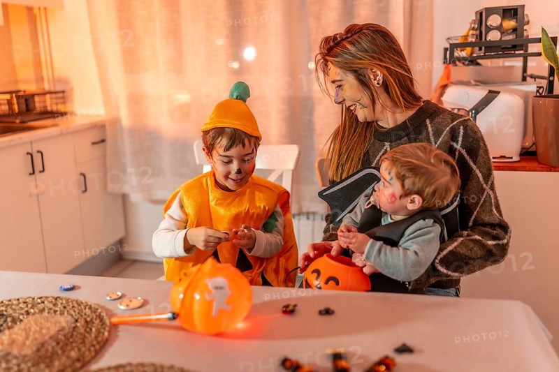 Mother and children wearing halloween costumes are sitting at the kitchen table and preparing for trick or treat