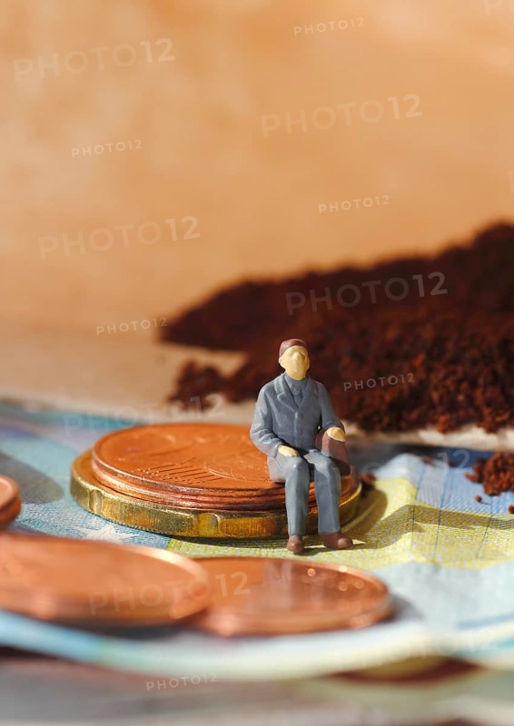 Miniature figure of a man sitting on coins and banknotes, ground coffee in a filter bag in the background, North Rhine-Westphalia, Germany