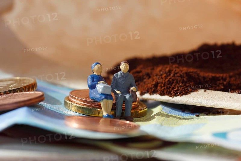 Miniature figure of a married couple sitting on coins and banknotes, ground coffee in a filter bag in the background, North Rhine-Westphalia, Germany