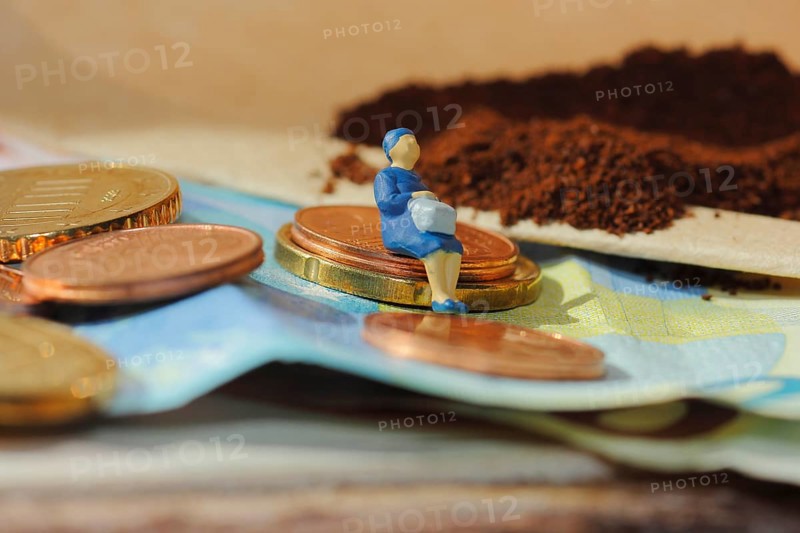 Miniature figure of a woman sitting on coins and banknotes, ground coffee in a filter bag in the background, North Rhine-Westphalia, Germany
