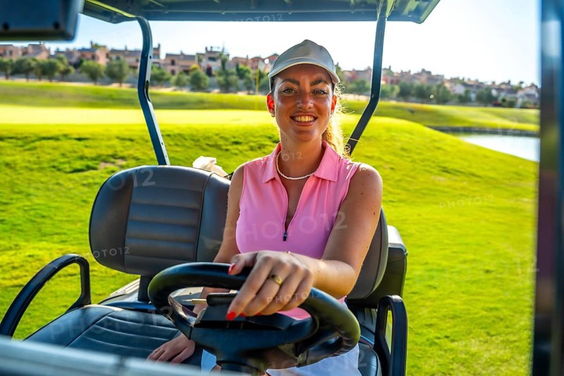 Smiling female golfer driving a golf cart across a sunny golf course, enjoying leisure time in the vibrant outdoors surrounded by lush greenery