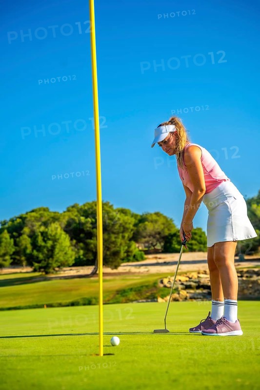 Professional golfer concentrating on the green, about to putt during a sunny day on a beautiful golf course