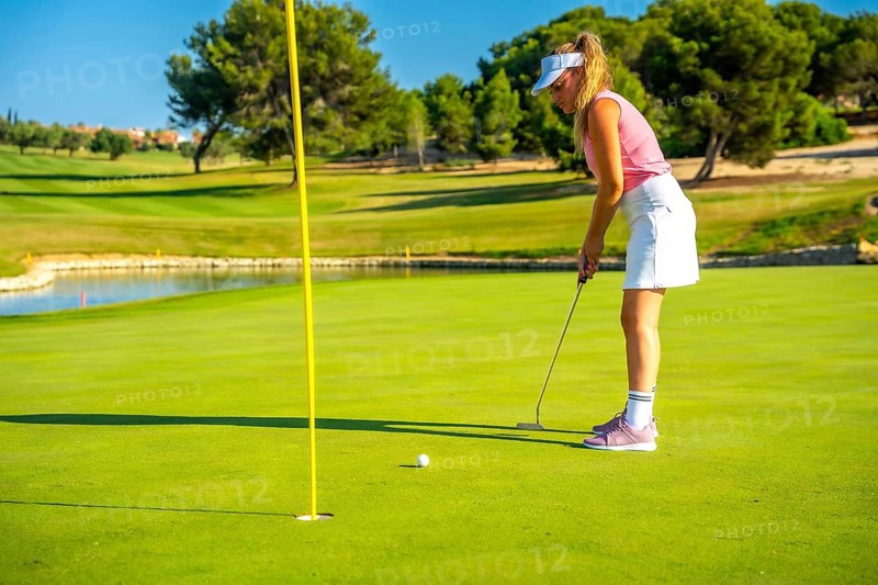 Professional golfer putting the ball on a sunny day, enjoying the beautiful scenery of a lush golf course surrounded by nature