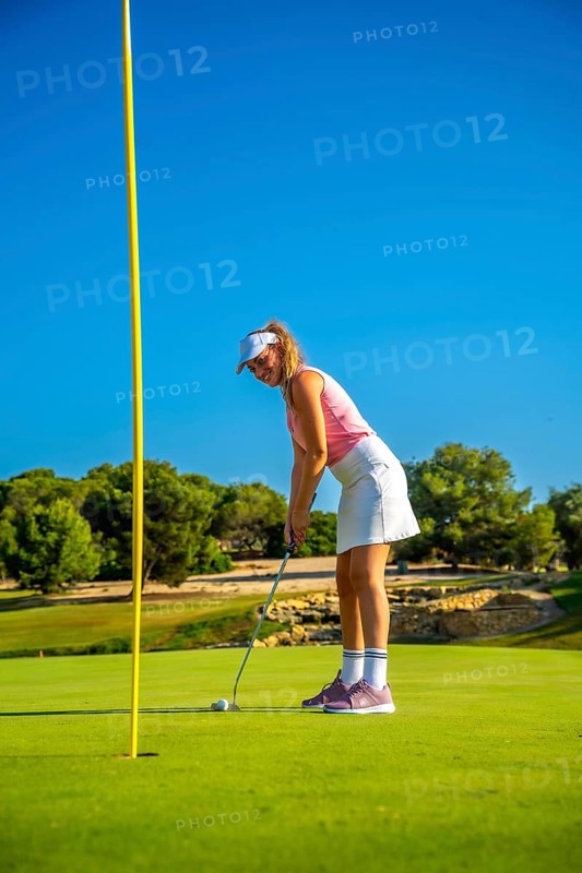 Female golfer putting the ball on the green under a bright sun, showcasing skill and precision on the lush course during summer