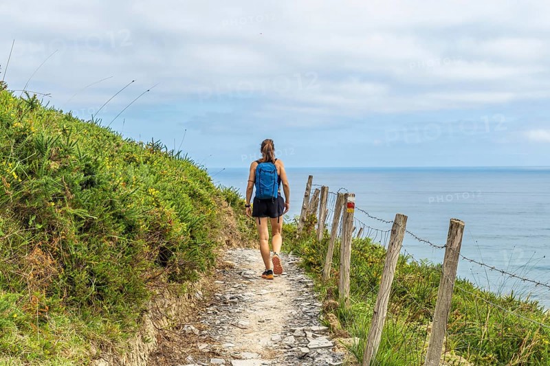 Female tourist walking along a coastal path in zumaia, basque country, enjoying the scenic view of the ocean