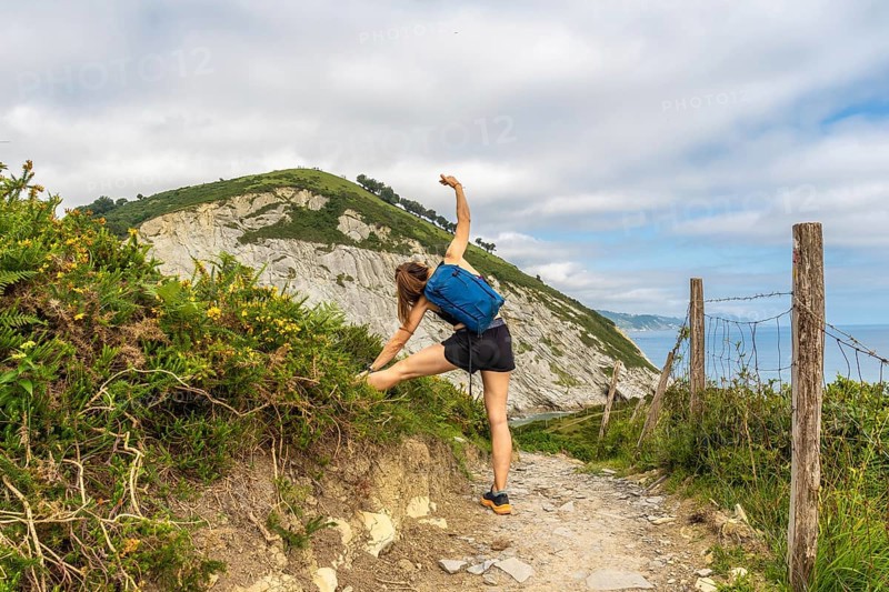 Female hiker stretching leg on a trail overlooking sakoneta beach and flysch cliffs in zumaia, gipuzkoa, basque country, spain