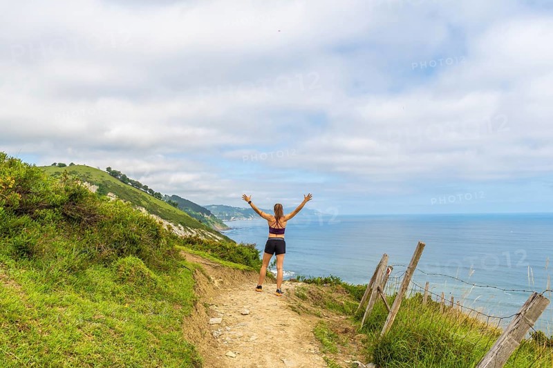 Woman hiker celebrating scenic coastal view with raised arms at sakoneta beach flysch cliffs in zumaia, gipuzkoa, basque country, spain