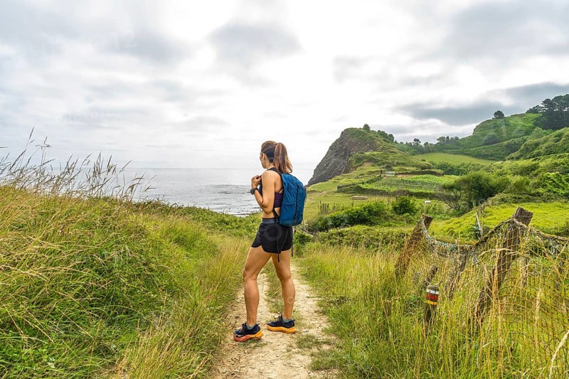 Female hiker enjoying the scenic view of sakoneta beach and its flysch cliffs in zumaia, gipuzkoa, during a summer hike in the basque country