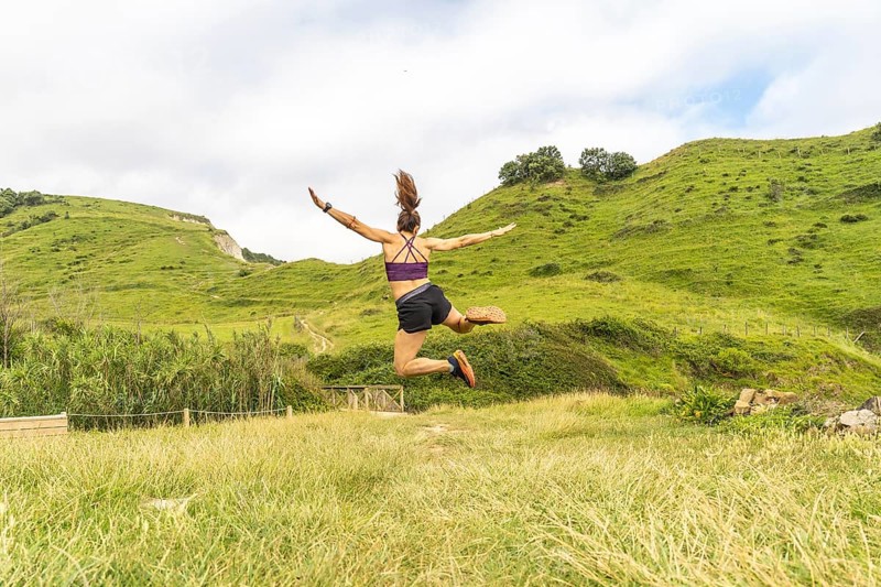 Sporty woman jumping with outstretched arms in a beautiful natural landscape in zumaia, gipuzkoa, celebrating achievement and freedom