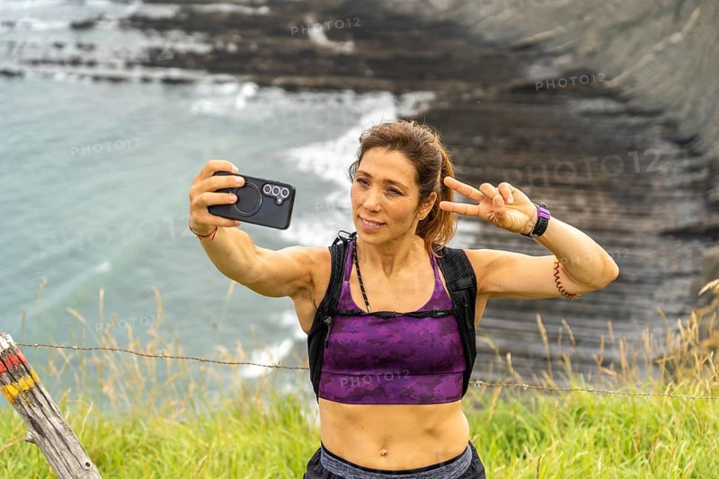 Female hiker taking a selfie with victory sign while hiking along the cliffs of sakoneta beach in zumaia, basque country, spain