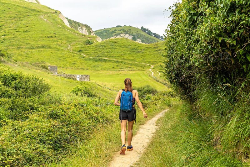 Female tourist walking on a path surrounded by lush vegetation, enjoying the scenic view of sakoneta beach and the flysch cliffs in zumaia, basque country