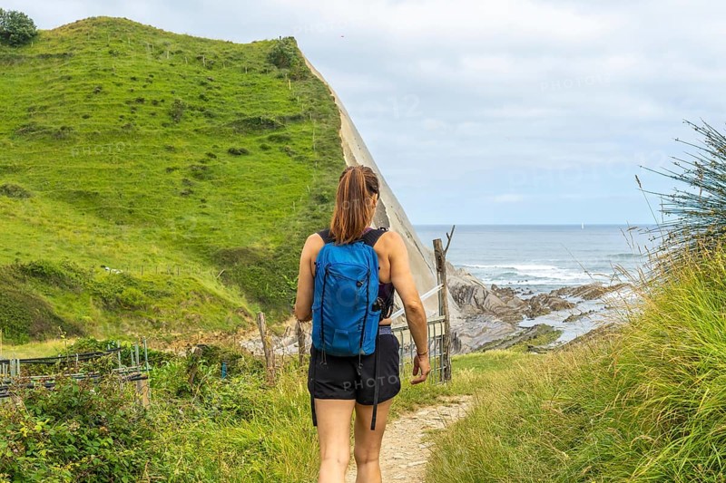Female tourist walking down a path towards sakoneta beach, enjoying the view of the flysch cliffs and the ocean