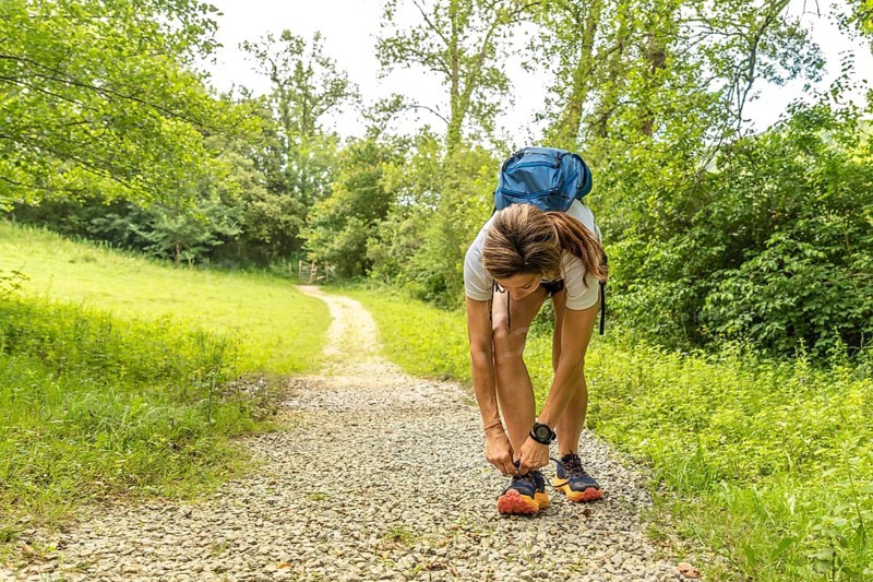 Female hiker tying her shoelaces before starting her trekking activity on a gravel path in a forest