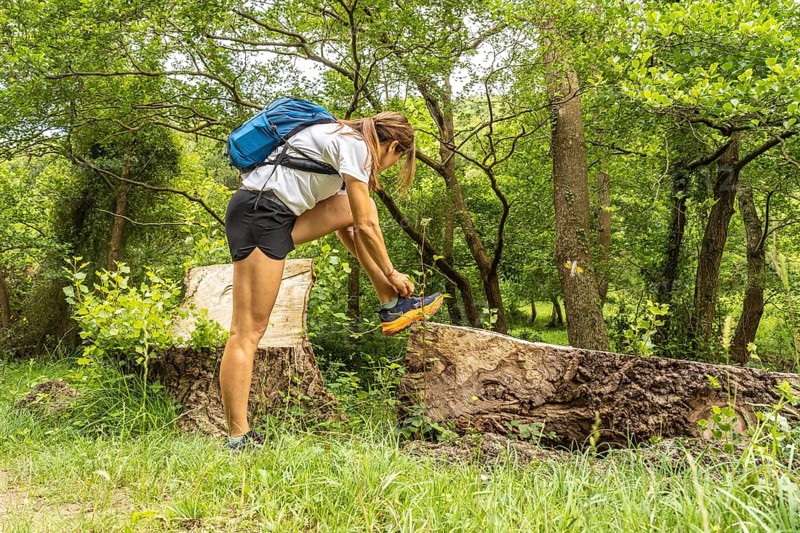 Female hiker tying her shoelaces while taking a break on a fallen tree trunk in a vibrant green forest