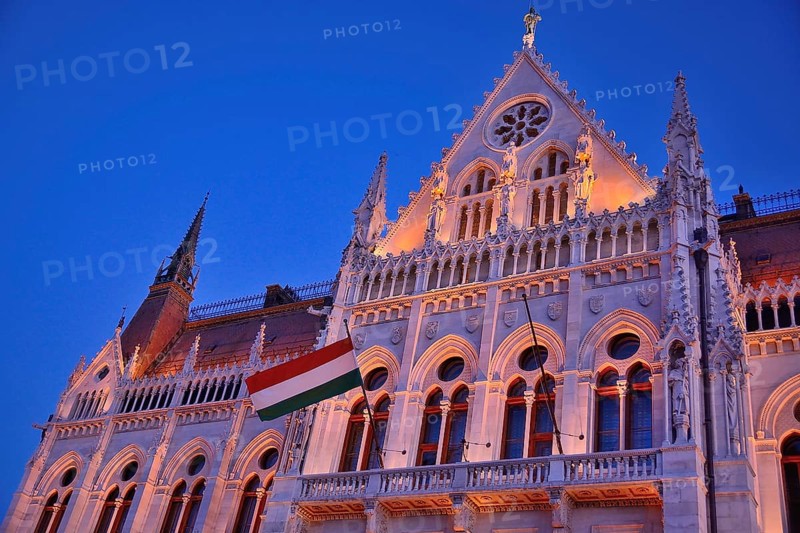 Ornate facade of hungarian parliament building illuminated at twilight with hungarian flag waving, budapest, hungary
