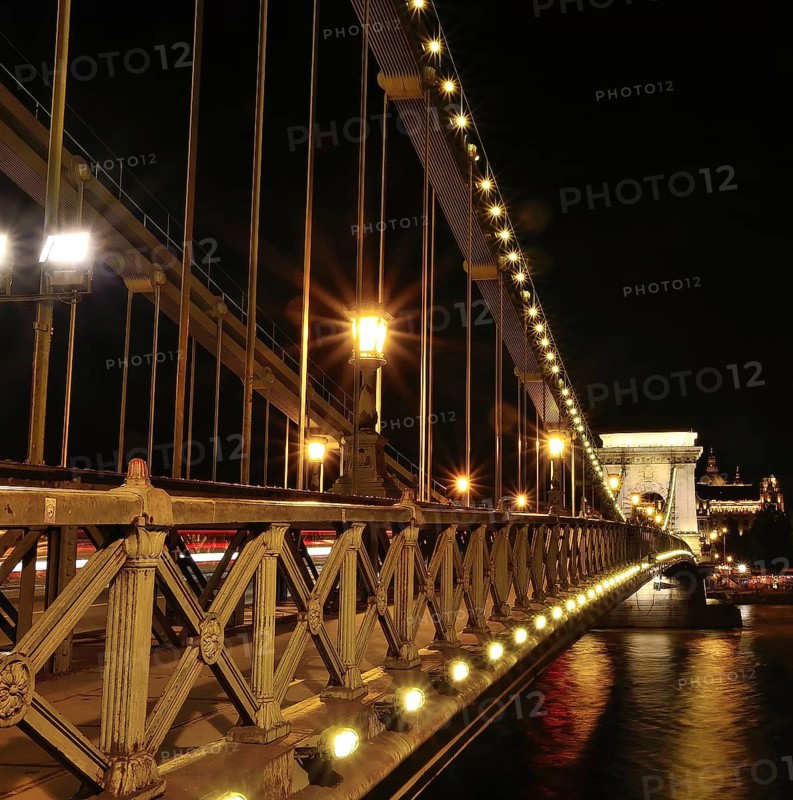 Chain bridge glowing beautifully at night, showcasing blurred car light trails against the backdrop of budapest's enchanting cityscape