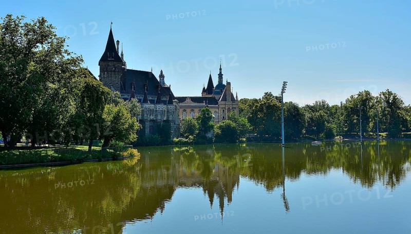 Vajdahunyad castle reflecting beautifully on the lake in budapest's city park, surrounded by lush trees on a sunny summer day