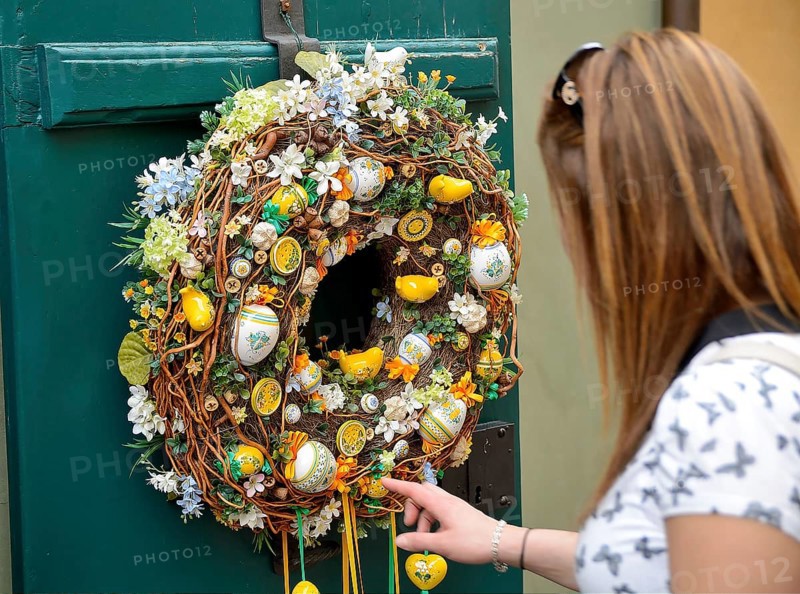 Tourist touching a colorful easter wreath with ceramic eggs and chicks hanging on a green door in prague or budapest