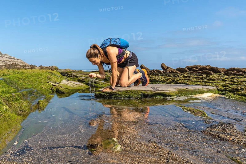 Female hiker refreshing with water from a puddle on the flysch rock formations of sakoneta beach in zumaia, basque country, spain