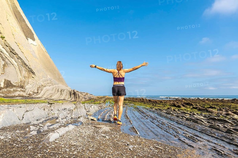 Female athlete enjoying freedom and nature, walking on the unique rock formations of sakoneta beach at low tide, with open arms towards the sea