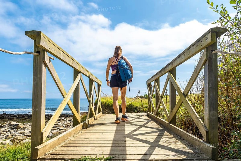 Hiker walking on a wooden walkway leading to sakoneta beach in zumaia, basque country, with flysch cliffs and blue sea in background