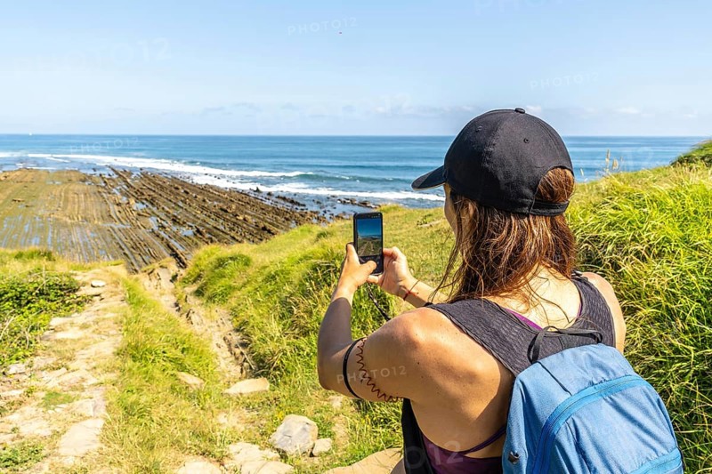 Hiker taking pictures of the impressive flysch cliffs at sakoneta beach in zumaia, basque country, spain, a unique geological formation