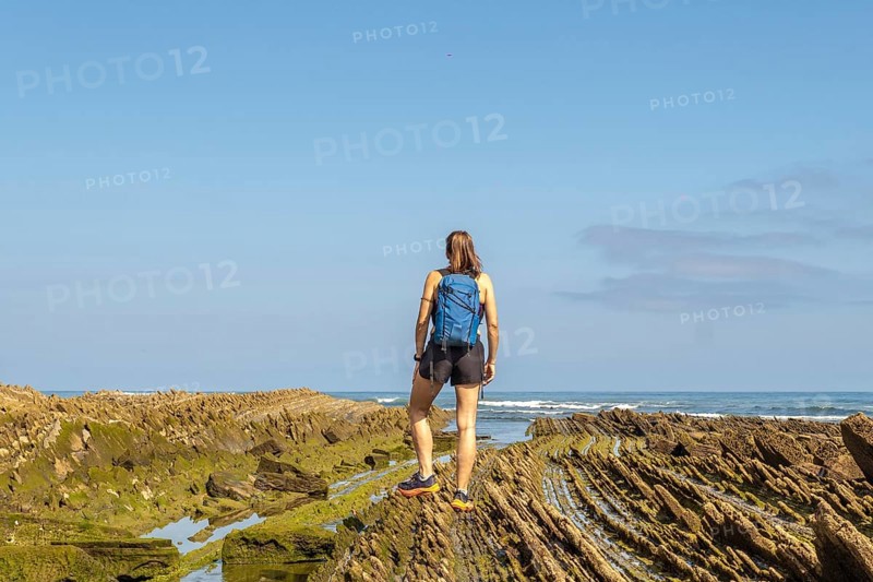 Female hiker with backpack admiring the stunning coastal rock formations of the zumaia flysch on sakoneta beach, gipuzkoa, basque country