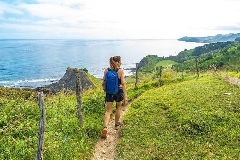 Female hiker enjoying the stunning view of sakoneta beach and its coastal flysch in zumaia, basque country, spain, during a sunny summer day