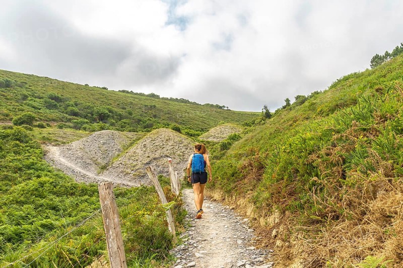 Female tourist walking on a hiking trail exploring the beautiful landscape near sakoneta beach in zumaia, basque country, on a cloudy summer day
