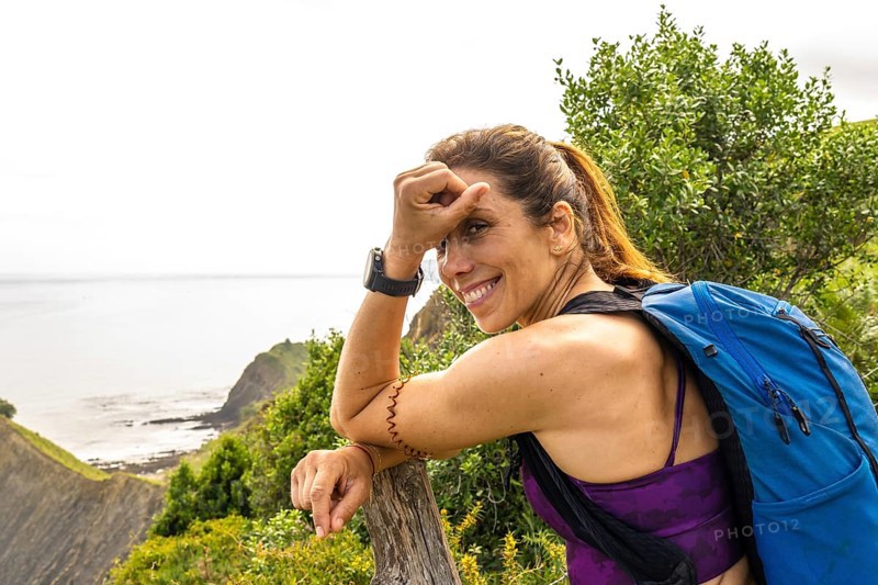 Female hiker with backpack taking a break and enjoying the breathtaking view of sakoneta beach and flysch cliffs in zumaia, basque country
