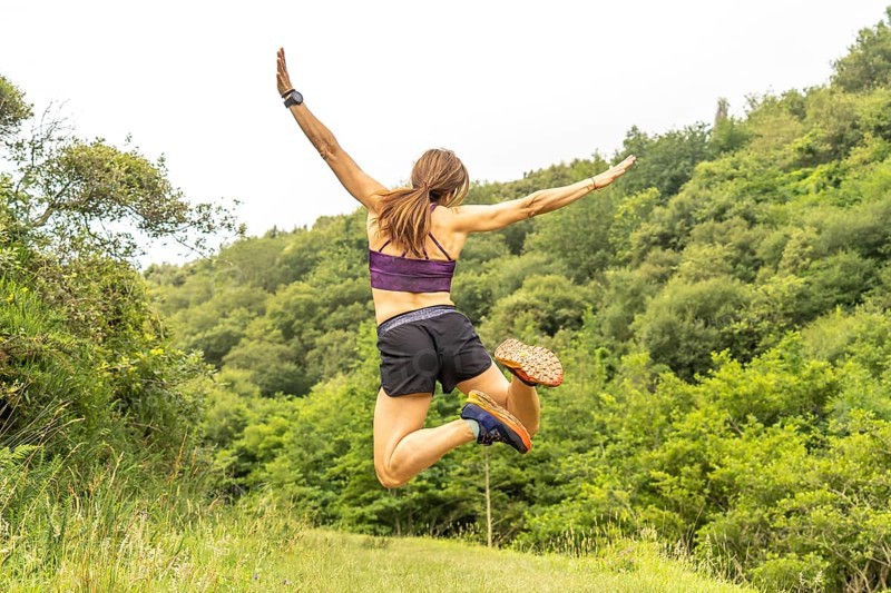 Celebrating athletic achievement, a woman jumps with outstretched arms amidst the verdant hills near sakoneta beach and the flysch cliffs of zumaia, gipuzkoa, in the basque country