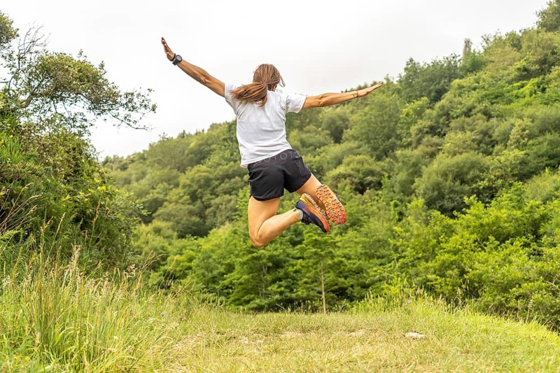 Celebrating athletic achievement, a female athlete jumps with outstretched arms in a vibrant green meadow near zumaia, basque country, expressing pure joy and freedom