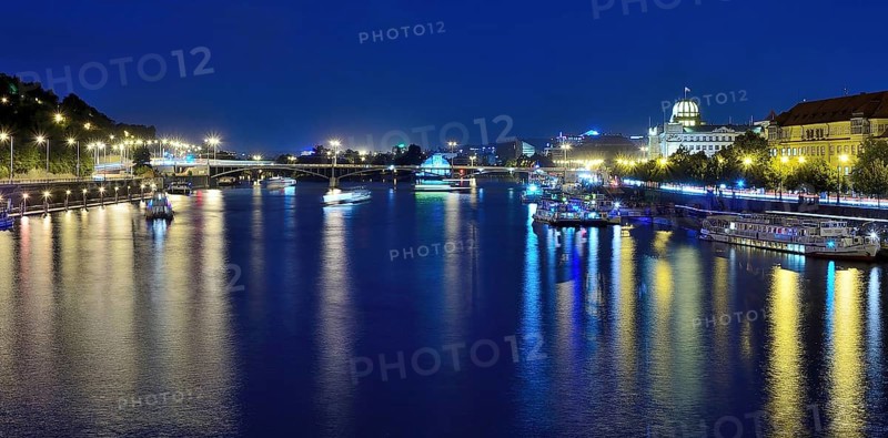 Vltava river reflecting the vibrant cityscape of prague, with boats sailing gracefully on a warm summer night, creating a serene atmosphere
