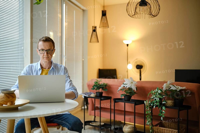 A man is focused on his laptop while seated at a small round table in a stylish living room