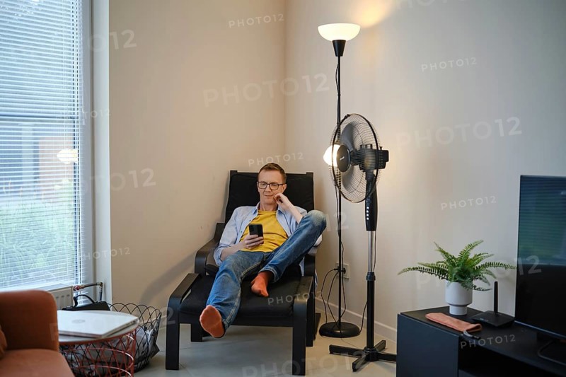 A middle-aged man is seated comfortably in a modern chair, casually browsing his smartphone