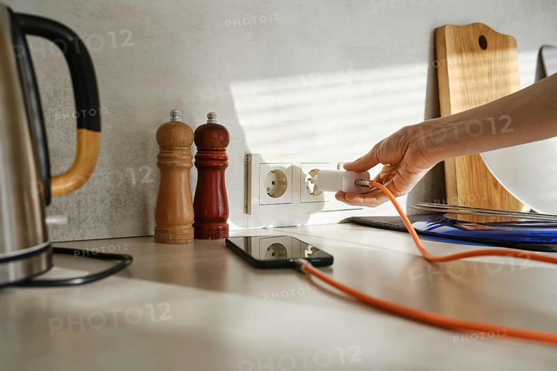 A person plugs a smartphone charger into an outlet while standing in a stylish kitchen